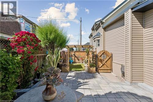 Paver patio with a decorative wooden gate and vibrant red flowering shrubs - 180 Campbell Avenue, Hamilton, ON - Outdoor With Deck Patio Veranda