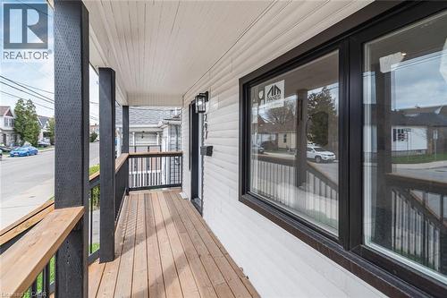Covered porch with wood-finish flooring, dark-stained railings, and white siding - 297 Britannia Avenue, Hamilton, ON 