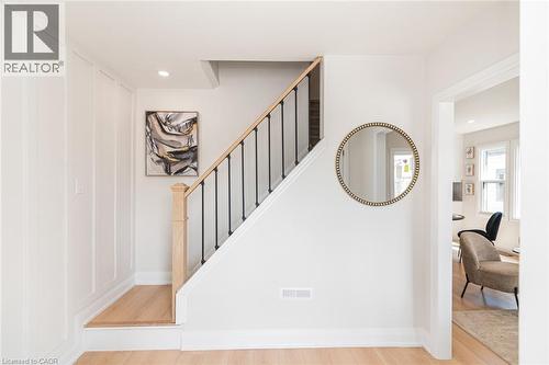 Light wood-finish flooring throughout, featuring a staircase with wood banister and black metal spindles - 297 Britannia Avenue, Hamilton, ON 