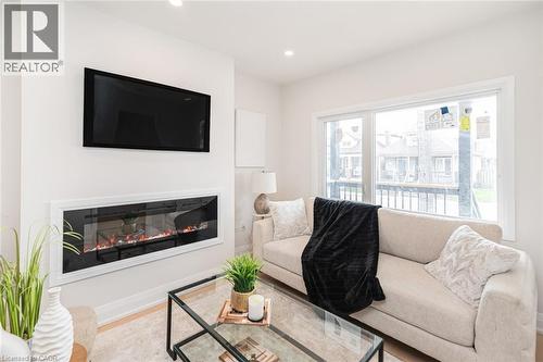 Contemporary living area featuring a wall-mounted linear electric fireplace beneath a mounted television - 297 Britannia Avenue, Hamilton, ON 