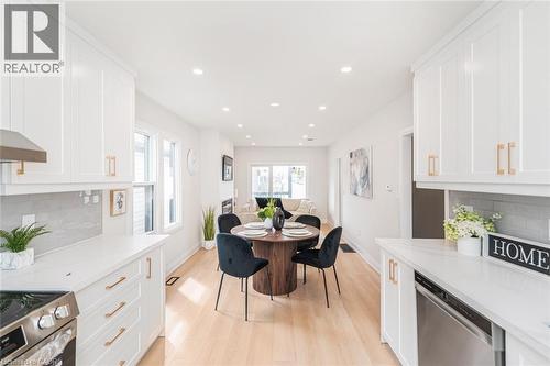 Bright, open-concept kitchen featuring white shaker cabinetry, light-toned wood-finish flooring, recessed lighting, stainless steel appliances, and quartz countertops with a subway tile backsplash - 297 Britannia Avenue, Hamilton, ON 