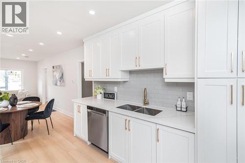 Kitchen featuring white cabinetry with gold-finish hardware, light grey subway tile backsplash, and light countertops - 297 Britannia Avenue, Hamilton, ON 