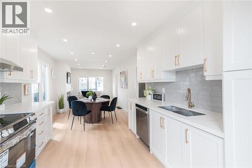 Bright open-concept kitchen featuring white shaker-style cabinetry, light-toned wood-finish flooring, recessed lighting, subway tile backsplash, and a stainless steel double sink - 297 Britannia Avenue, Hamilton, ON 