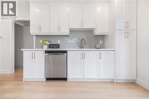 Kitchenette featuring white shaker-style cabinetry, a stainless steel dishwasher, white countertops, a gray subway tile backsplash, and wood-finish flooring - 297 Britannia Avenue, Hamilton, ON 