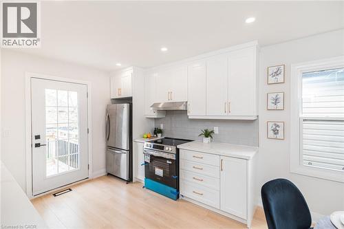 Modern kitchen with light wood-finish flooring, white cabinetry with gold-tone hardware, and a subway tile backsplash - 297 Britannia Avenue, Hamilton, ON 