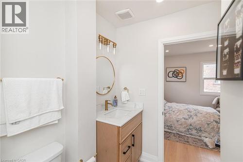Bathroom featuring a wood-finish vanity with a white countertop and integrated sink, complemented by a gold-finish faucet and circular mirror - 297 Britannia Avenue, Hamilton, ON 