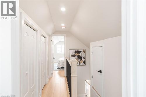 Upper-level hallway featuring light wood-finish flooring, white paneled doors, recessed lighting, and sloped ceilings - 297 Britannia Avenue, Hamilton, ON 