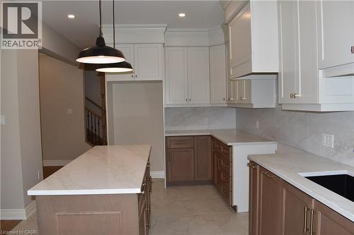 Spacious kitchen featuring white cabinetry, wood-finish lower cabinets, quartz countertops, stainless steel appliances, a large center island with seating, pendant lighting, recessed ceiling lights, a - 8 Dunlop Road, Hamilton, ON - Indoor Photo Showing Kitchen
