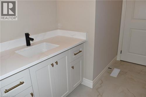Elegant primary bathroom vanity featuring a white shaker-style cabinetry with brass hardware, quartz countertop, rectangular undermount sink, and matte black wall-mounted faucet - 8 Dunlop Road, Hamilton, ON - Indoor