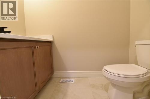 Clean, functional bathroom featuring a white porcelain toilet with soft-close seat, wood-finish vanity with dual handles, ceramic tile flooring, and neutral wall finishes - 8 Dunlop Road, Hamilton, ON - Indoor Photo Showing Bathroom