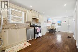 Open concept kitchen featuring cream-colored cabinetry, stone-finish countertops, stainless steel appliances, and wood-finish flooring - 