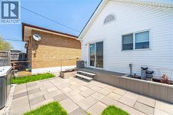 Expansive backyard featuring a paver patio with integrated green spaces, a raised composite deck, and white vinyl siding - 