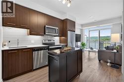 Open-concept living space featuring wood-finish flooring, a kitchen with dark wood cabinetry and stainless steel appliances, a white subway tile backsplash, and a movable dark kitchen island - 