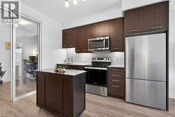 Contemporary kitchen featuring wood-finish flooring, dark wood cabinetry, white subway tile backsplash, and stainless steel appliances - 