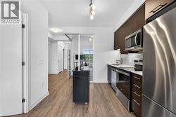 Modern kitchen featuring stainless steel appliances, dark wood-finish cabinetry, light-toned countertops, and a subway tile backsplash - 