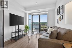 Open-concept living space with wood-finish flooring, a full-height glass sliding door to the balcony, and distant green hills - 