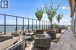Rooftop terrace featuring expansive water scenery, glass and metal railing, square planters with trees, and a built-in outdoor grilling station - 