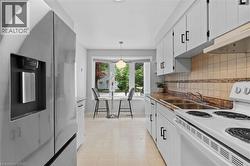 Galley kitchen featuring white cabinetry with black hardware, a stainless steel refrigerator, white electric range, and a dual basin stainless steel sink - 