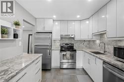 Contemporary kitchen featuring white flat-panel cabinetry, stainless steel appliances, patterned stone countertops, and a coordinating stone backsplash - 