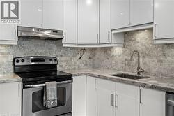 Modern kitchen featuring light gray cabinetry, stainless steel appliances, a tile backsplash, and stone countertops - 