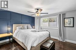 Feature wall with decorative paneling, wood-finish flooring, ceiling fan with integrated lighting, window with blinds, and light gray wall paint - 