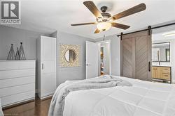 Bedroom featuring wood-finish flooring, a ceiling fan with light fixture, and a decorative barn door - 