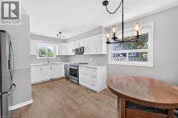 Bright kitchen featuring white cabinetry, light countertops, subway tile backsplash, wood-finish flooring, and a contemporary multi-light chandelier - 