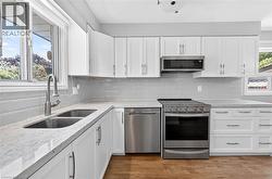 Contemporary kitchen featuring white cabinetry, light-toned countertops, a stainless steel appliance suite, subway tile backsplash, and wood-finish flooring - 