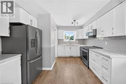 Galley kitchen featuring white cabinetry, light countertops, wood-finish flooring, stainless steel appliances, and a subway tile backsplash - 