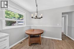 Dining area featuring wood-finish flooring, a contemporary chandelier, two-tone wall treatment with chair rail molding, and a bright window - 