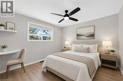 Bedroom featuring neutral wall colors, wood-finish flooring, a contemporary ceiling fan with integrated lighting, a built-in wall shelf, and a window with roller blinds - 