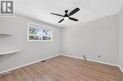 Spacious room featuring wood-finish flooring, light gray wall paint, and a modern black ceiling fan with integrated lighting - 