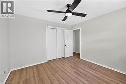 Spacious room featuring wood-finish flooring, light gray walls, a black ceiling fan, white baseboards, and a sliding closet door - 