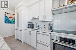 Contemporary kitchen featuring white high-gloss cabinetry with brushed nickel hardware, light-toned stone countertops, and a white subway tile backsplash - 