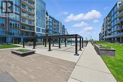 Expansive outdoor courtyard featuring a modern black pergola, paver stone patio, concrete walkways, and landscaped garden beds - 
