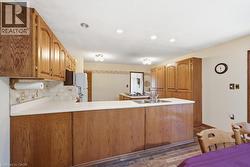 Kitchen featuring wood-finish cabinetry, white countertops, a double basin sink, recessed ceiling lighting, and wood-finish flooring - 