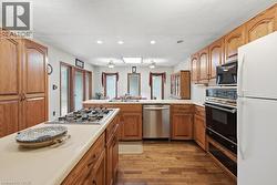 Kitchen featuring wood-finish flooring, wood cabinetry, light countertops, a built-in oven, and a gas cooktop - 