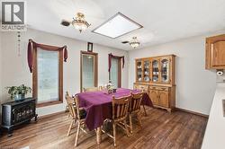 Dining area featuring wood-finish flooring, a built-in wood hutch, multiple windows with wood trim, a ceiling-mounted skylight, and decorative light fixtures - 