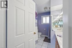 Bathroom featuring white square tile flooring, a window with privacy glass, a white toilet, and a vanity with a white countertop and wood-finish cabinetry - 
