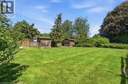 Expansive lawn featuring two storage sheds, mature trees, and perimeter fencing - 