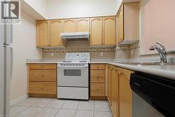 Kitchen featuring wood-finish cabinetry, light-toned countertops, tile flooring, and a decorative tile backsplash - 