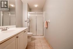 Bathroom featuring a single vanity with a white countertop and base cabinetry, a toilet, a shower with a sliding glass door, and tiled flooring - 