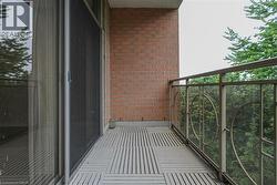 Private balcony featuring brick siding, slat-style flooring, a sliding glass door with screen, and a decorative metal railing with clear panels - 