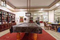 Recreation room featuring a billiards table with a suspended light fixture, extensive built-in wooden shelving, and large paneled windows - 
