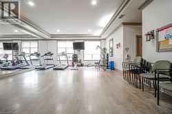 Spacious fitness area featuring wood-finish flooring, a mirrored wall, multiple windows, recessed lighting, and crown molding - 