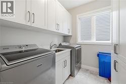 Laundry room featuring white shaker cabinetry, an integrated utility sink, white countertops, and light gray tiled flooring - 