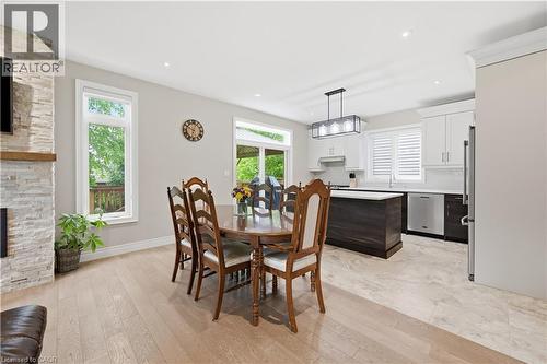 Open-concept living space featuring wood-finish flooring, a stacked stone fireplace with a wood mantel, and large windows - 1 Lindsay Way, Grimsby, ON - Indoor Photo Showing Dining Room With Fireplace
