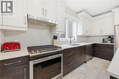 Modern kitchen featuring white upper cabinetry, dark wood-finish lower cabinetry, and light-toned countertops - 1 Lindsay Way, Grimsby, ON - Indoor Photo Showing Kitchen With Double Sink