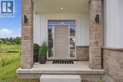 Entryway featuring a panel door with transom window, stone veneer columns, vertical siding, and a concrete porch - 
