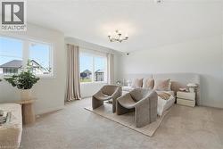 Spacious room featuring broadloom carpeting, multiple windows providing natural light, a contemporary chandelier, and a neutral color palette - 
